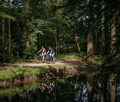 Zwei Personen fahren mit ihren Fahrrädern an einem Fluss entlang 